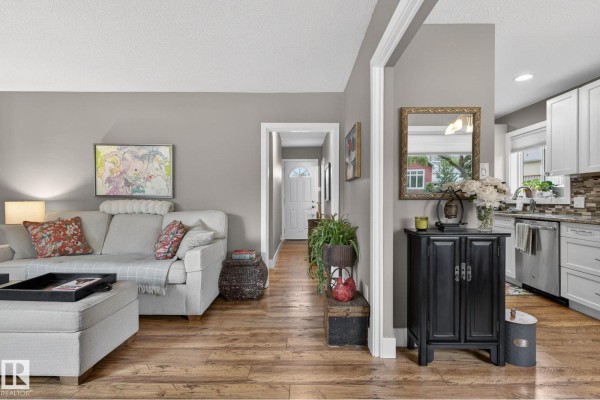 Living room with neutral walls, light-colored sofa and ottoman, wood floors, and view into the kitchen. - 10108 144 St Nw, Edmonton