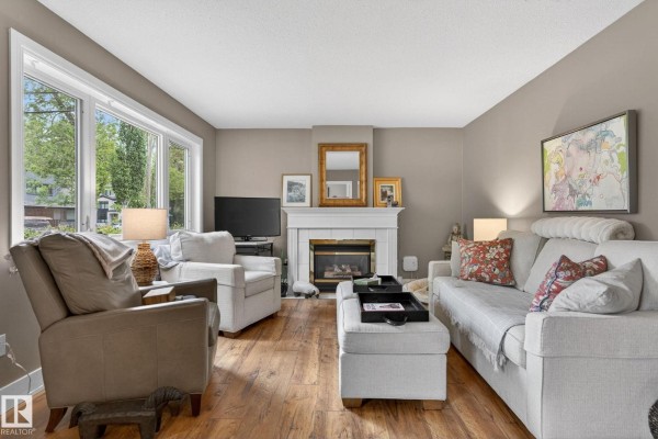 Living room with a fireplace, large bay window, two armchairs, sofa, and wood laminate flooring. - 10108 144 St Nw, Edmonton