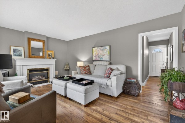 Living room with a fireplace, sofa, ottomans, and a view down a hallway towards the front door. - 10108 144 St Nw, Edmonton