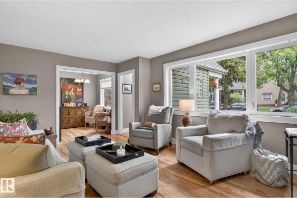 Living room with comfortable seating, a large window overlooking the street, and an opening to another room. - 10108 144 St Nw, Edmonton