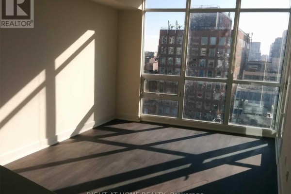Empty room with dark wood floors, large windows overlooking city buildings, and bright sunlight. - 1011 - 30 Roehampton Avenue, Toronto