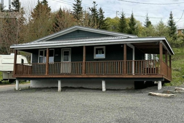Open-concept living space with wood floors, white cabinets, refrigerator, and a wall-mounted air conditioning unit. - 1011 East Margaree Road, Margaree