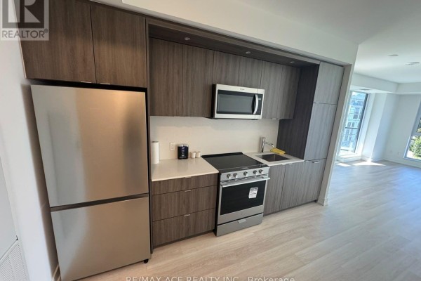 View of the kitchen with dark wood cabinets, stainless steel refrigerator, stove, and microwave. - 1012 - 25 Cordova Avenue, Toronto