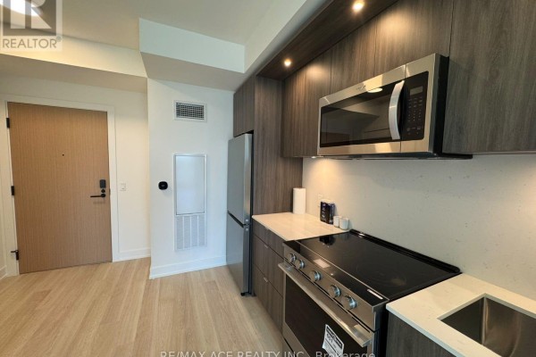 Galley kitchen with dark gray cabinetry, stainless steel appliances, and light laminate flooring. - 1012 - 25 Cordova Avenue, Toronto