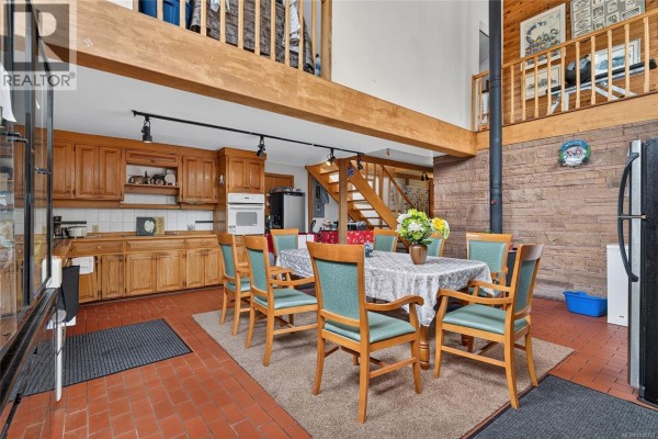Dining room with a wooden table, chairs, brick wall, and tiled floor. - 1012 Fairdowne Rd, Errington