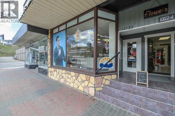 Street-level view of a commercial building with stone accents and large glass windows displaying political and business signage. - 10122/24 Main Street, Summerland