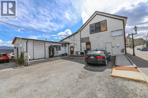 Rear exterior view of white commercial buildings with a parking lot, a car, and a ramp leading to a side entrance. - 10122/24 Main Street, Summerland