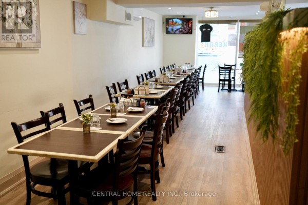 View of a restaurant dining room with tables and chairs, and a large green plant. - 10123 Yonge Street, Richmond Hill