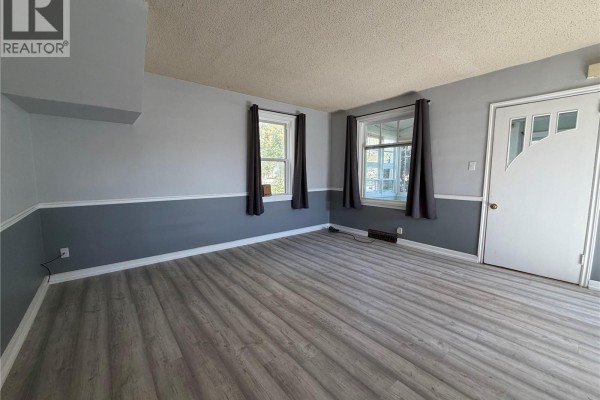 Interior view of a living room with two windows, a front door, and grey curtains. - 1014 6th Avenue Nw, Moose Jaw