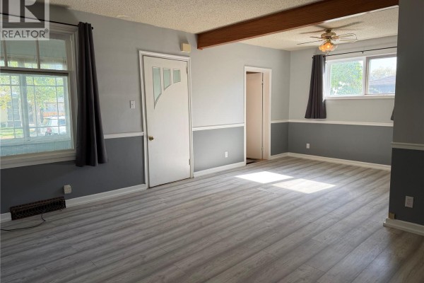 Interior view of a living room showing a door, windows, and a wood beam on the ceiling. - 1014 6th Avenue Nw, Moose Jaw