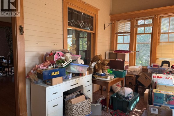 Sunroom with wood trim, windows, and clutter, showing a desk and boxes. - 1014 Iroquois Street W, Moose Jaw