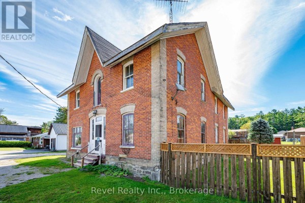 Side view of a red brick house with a wooden fence and green lawn. - 1014 Portage Road, Kawartha Lakes