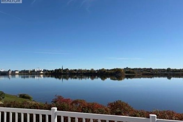 Calm blue water reflects a town skyline with a church steeple under a clear blue sky. - 1015 Winton Crescent, Bathurst