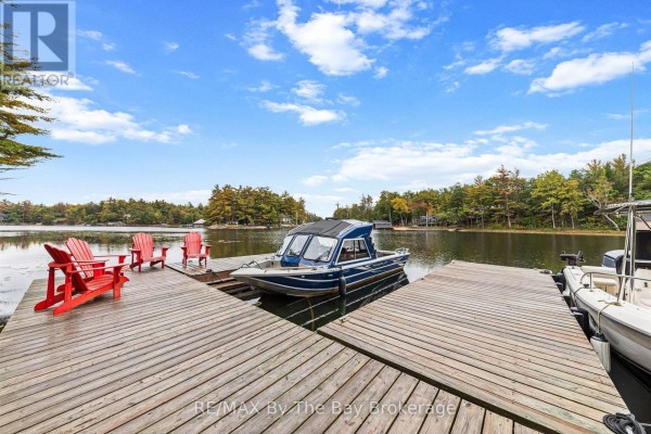 Wooden dock with red chairs and moored boats, featuring a view of the lake. - 10158 Georgian Bay Shore, Georgian Bay