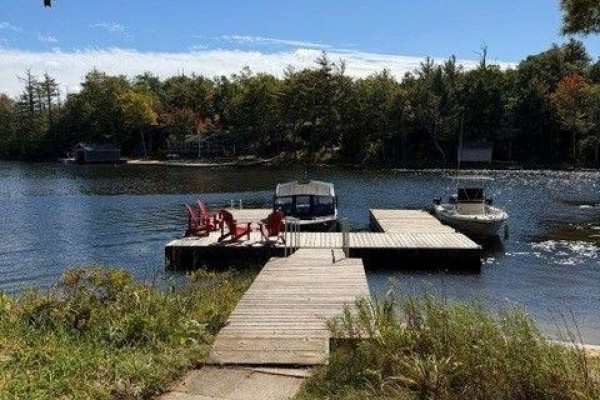 Wooden dock extending into the water with boats and chairs, surrounded by greenery. - 10158 Georgian Bay Shore, Georgian Bay