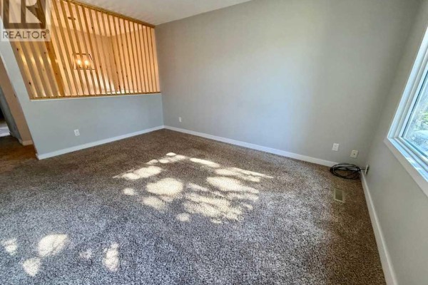 Living room with beige carpet and partition wall. - 1016 20 Avenue, Coaldale