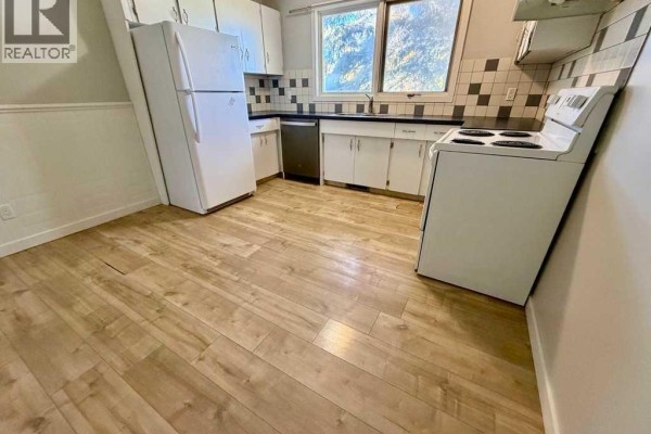 Kitchen with white cabinets, checkered backsplash, white appliances, and wood-look flooring. - 1016 20 Avenue, Coaldale