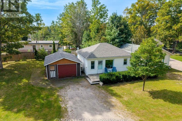 Exterior view of a white bungalow with a detached garage and a small front porch with two blue chairs. - 1016 Mill Street, Muskoka Lakes