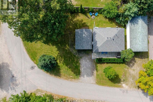 Overhead drone shot of the residential property, showing the bungalow, attached garage, and surrounding lawn. - 1016 Mill Street, Muskoka Lakes
