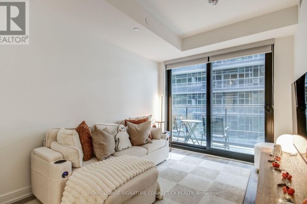 Living room with a beige sofa, ottoman, checkered rug, and large glass door to a balcony. - 1017 - 1 Jarvis Street, Hamilton