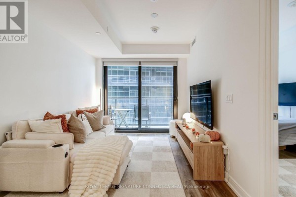 Living room with a sofa, television on a wooden media console, and a view of the balcony. - 1017 - 1 Jarvis Street, Hamilton