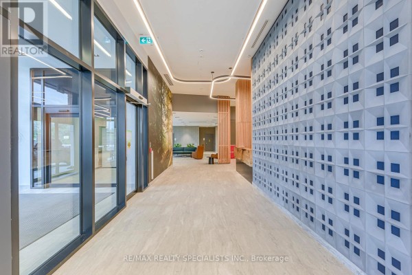 Building lobby with glass doors, textured wall panels, and modern lighting. - 1018 - 2485 Eglinton Avenue, Mississauga