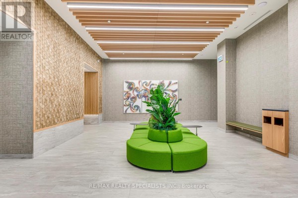 Lobby seating area with a circular green sofa, plants, and abstract artwork. - 1018 - 2485 Eglinton Avenue, Mississauga
