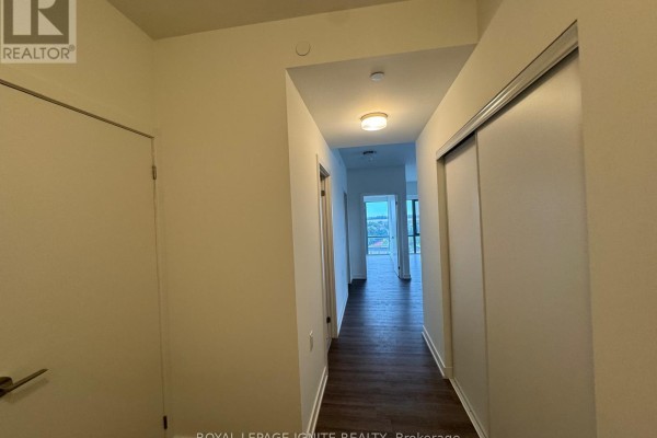 Interior hallway with white walls, dark wood floors, sliding closet doors, and view into rooms. - 1018 - 51 Clarington Boulevard, Clarington