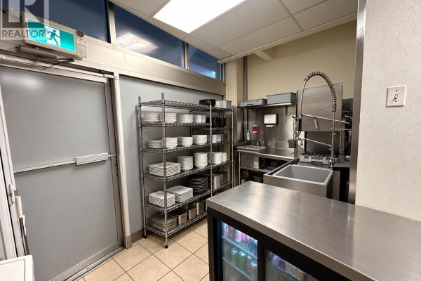 Restaurant back area with a commercial sink, drying rack holding plates, and a refrigerated beverage display. - 1018 4500 Kingsway, Burnaby