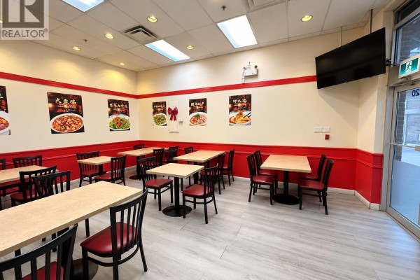 Dining area with light wood floors, red banquettes, tables, and chairs, and posters on the walls. - 1018 4500 Kingsway, Burnaby