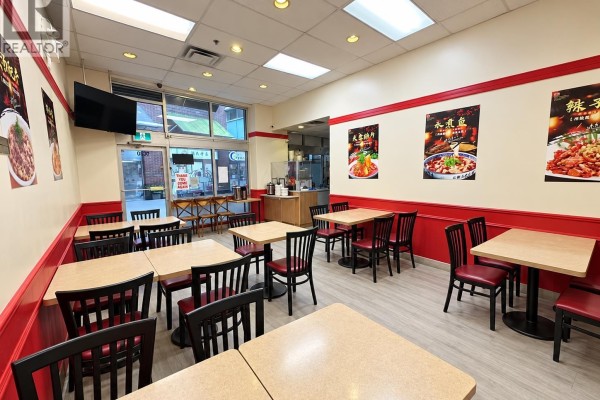 Restaurant dining room with tables and chairs, red trim, and large windows looking onto the street. - 1018 4500 Kingsway, Burnaby