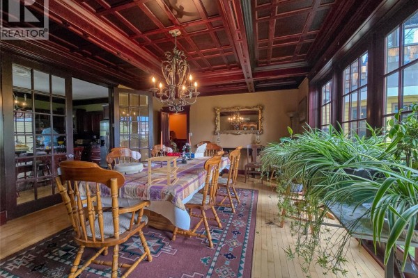 Dining room with a large table, wooden chairs, ornate chandelier, and sunroom with plants. - 1018 5th Street, Invermere