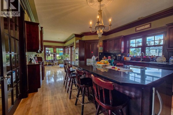 Large kitchen island with granite countertop and bar stools, dark wood cabinets, and hardwood floors. - 1018 5th Street, Invermere