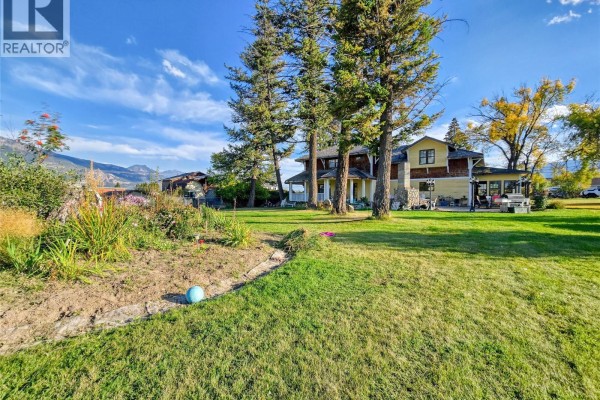 View of the house from the backyard, showing grass, trees, and mountains in the background. - 1018 5th Street, Invermere