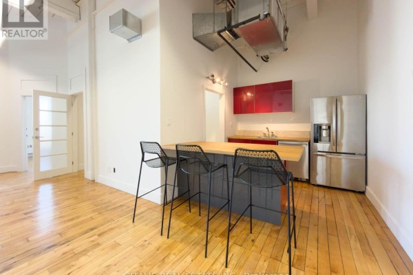 Gym interior with cardio equipment, wood floors, large windows, and yellow accent wall. - 101a - 219 Dufferin Street, Toronto