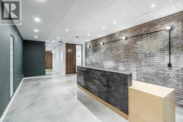 Commercial building entrance lobby with tiled floor, metal staircase, glass doors, and exterior view. - 102, 10820 24 Street Se, Calgary