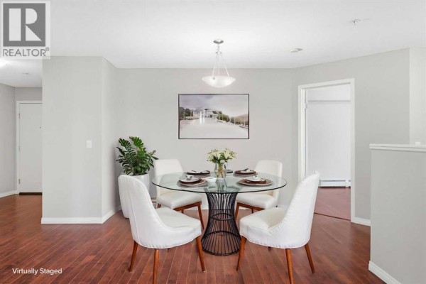 Dining room with a glass-top table, white chairs, and dark hardwood floors. - 102, 17 Country Village Bay Ne, Calgary