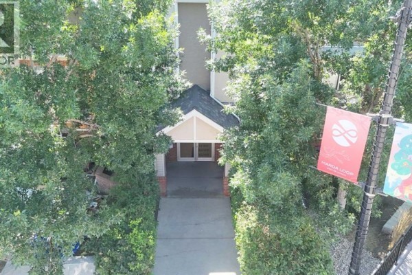Close-up exterior view of an apartment building entrance with double doors and trees. - 102, 1811 34 Avenue Sw, Calgary