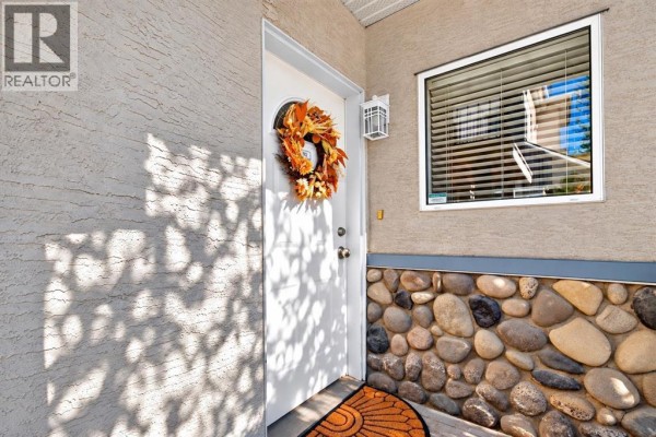Front entrance of a townhouse with a white door, window, and stone base. - 102, 622 56 Avenue Sw, Calgary