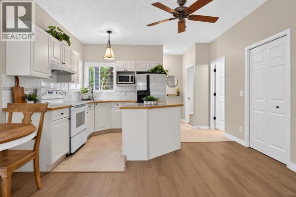Bright white kitchen with an island, stainless steel appliances, and dining area. - 102, 622 56 Avenue Sw, Calgary