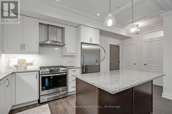 Kitchen with white cabinets, stainless steel appliances, granite countertops, and a dark wood island. - 102 - 128 Garden Drive, Oakville