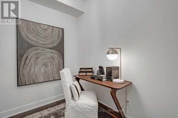 Small office nook with a wooden desk, white chair, and abstract wall art. - 102 - 128 Garden Drive, Oakville