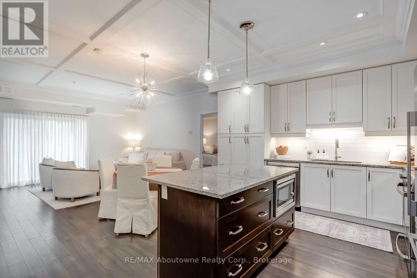 Open concept living and kitchen area with white cabinets, island, dining table, and living room furniture. - 102 - 128 Garden Drive, Oakville