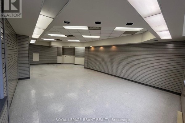 Large, empty commercial interior with gray slatwall panels and fluorescent lighting. - 102 - 139 Grand River Street N, Brant