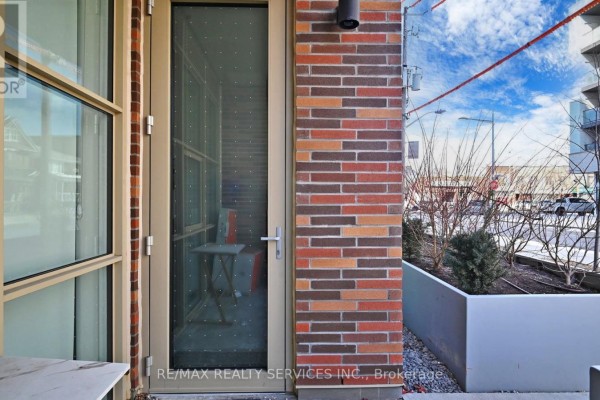 Apartment entrance door with a glass pane and brick exterior wall. - 102 - 1787 St. Clair Avenue W, Toronto
