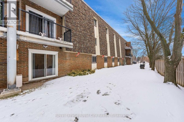 Close-up of the ground area with snow, grass, and sliding door access to the apartment - 102 - 234 Willow Road, Guelph