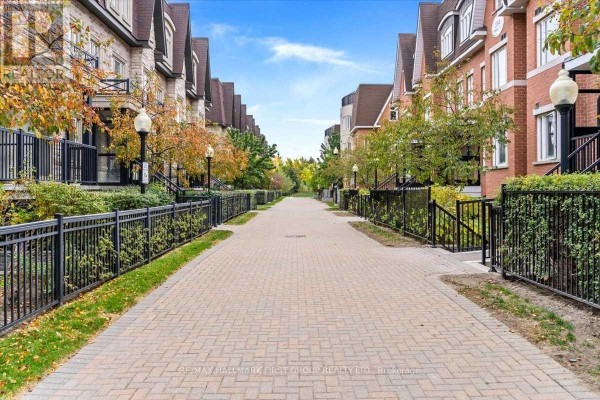 Paved walkway lined with black metal fences and townhouse exteriors. - 102 - 320 John Street, Markham