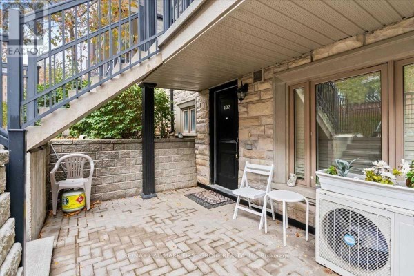 Ground floor entrance with a black door, stone facade, and concrete patio. - 102 - 320 John Street, Markham
