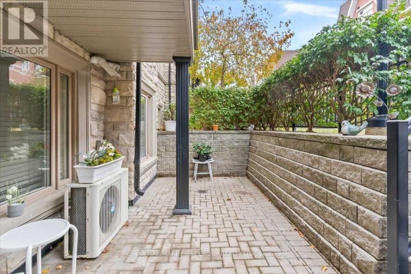 Concrete patio area with stone retaining walls and an outdoor air conditioning unit. - 102 - 320 John Street, Markham