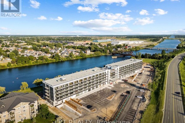 Aerial view of a modern apartment building complex next to a wide blue river and road. - 102 - 350 Prince Charles Drive S, Welland